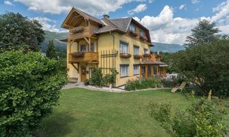 A beautiful yellow house with balconies and a large garden. The sky is clear and slightly cloudy.