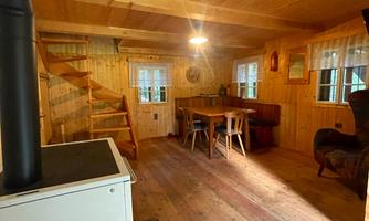 A cozy wooden house with an open living area. There is a staircase, a dining table, and a wood stove.