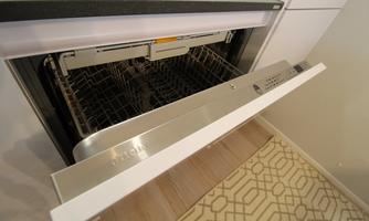 A modern dishwasher with an open door and empty dish racks. The floor is covered with an elegant carpet pattern.