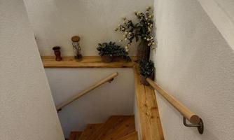 A wooden staircase with a bright wall and a wall lamp. Decorative plants and small accessories are on the stairs.