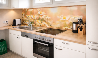 A modern kitchen with light wood and white furniture. The wall is decorated with a colorful floral motif.
