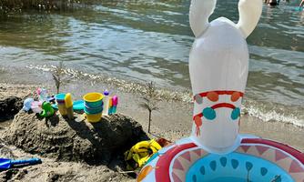 An inflatable toy with ears stands by the shore of a lake. In the background, people are visible in the water and toys for the sand.