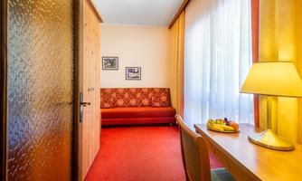 A cozy room with a red sofa and a desk. Bright curtains let in a lot of light.