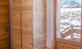 A modern entrance area with a wooden cabinet and a bench. A view of the mountains is visible through the window.
