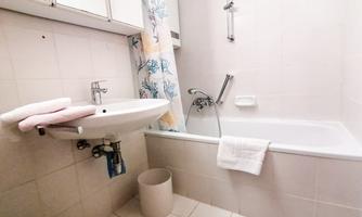 A bathroom with a bathtub, a sink, and a large mirror. Two towels and a trash can are visible.