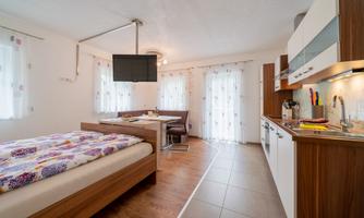 A modern room with a double bed and a kitchenette. Large windows provide plenty of daylight.
