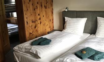 A cozy bedroom with two single beds and wooden walls. White bed linen and green towels are laid on the beds.