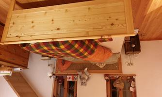A cozy bedroom with a bed made of light wood and a checkered blanket. On the bed lies a stuffed animal and there are several wooden pieces of furniture in the room.