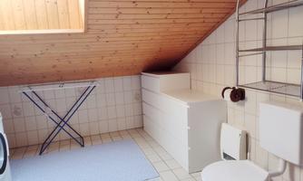 A bright bathroom with a sloped ceiling. It contains a toilet, a washing machine, and a clothes dryer.