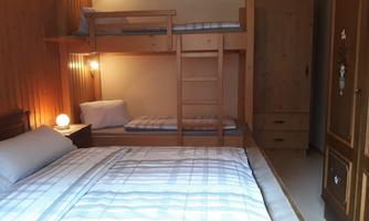 A simple bedroom with a double bed and a bunk bed. The room has wooden walls and a cozy atmosphere.