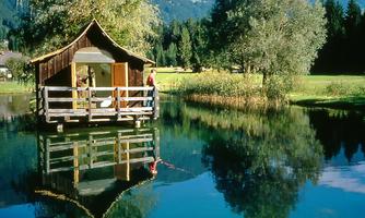 A beautiful wooden house by the water with a clear reflection in the lake. Surrounded by trees and a picturesque landscape.