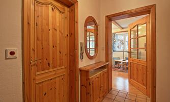 A cozy hallway with wooden paneling and tiled floor. On the left side, there is a wooden paneled door, and in the background, you can see another room.