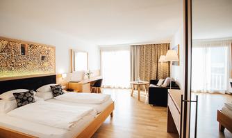A modern hotel room with two single beds and a cozy seating area. Large windows provide plenty of daylight and a view outside.