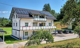 A modern house with solar panels and several balconies.  
Surrounded by green spaces and parked cars.