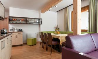 A modern kitchen corner with a dining area and large windows. The room has bright wooden furniture and a cozy atmosphere.