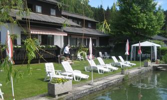 A quiet garden by the water with deck chairs and a pavilion. In the background, there are charming buildings and plenty of greenery.