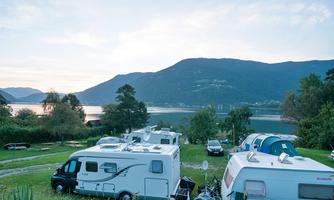 A beautiful campsite by the lake with RVs. In the background, there are mountains and a clear sky.