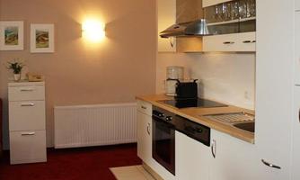 A modern kitchen with white furniture and wooden details. There is a stove, a sink, and some decorative elements on the wall.