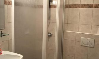 A modern bathroom with a shower cabin, a sink, and a toilet. The walls are tiled and the light is bright.