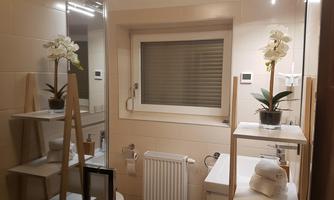 A modern bathroom with a white wall and light tiles. There are plants, shelves, and a mirror that makes the room appear larger.