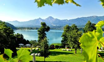 A tranquil lake surrounded by mountains and green trees. On the lawn, loungers and umbrellas are set up, inviting relaxation.