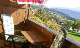 A cozy balcony with two chairs and a table. In the background, green hills and a beautiful landscape can be seen.