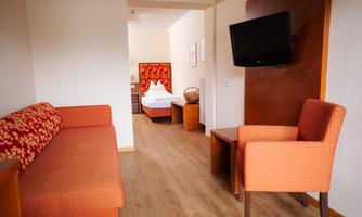 A cozy room with a red sofa and a television on the wall. In the background, you can see a bedroom with a double bed.