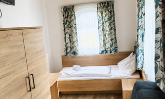 A cozy room with a single bed and a sofa bed. The walls are light, and the windows have curtains with a floral pattern.