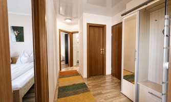 A bright hallway with wooden details and a carpet in warm colors. On the left side, a bedroom with a large bed is visible. Separate bathroom and toilet.