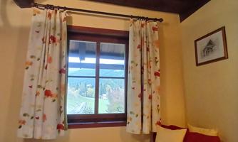A cozy room with a single bed and decorative pillows. The window offers a view of the outdoors, while the curtains are adorned with a pretty floral pattern.