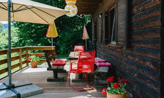 An inviting terrace with wooden cladding and colorful chairs. Flowers in pots and sunshades create a cozy atmosphere.