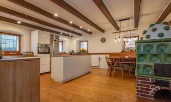 A modern kitchen with wooden floor and exposed beams. The room is bright and friendly, with a large dining table and a cozy sitting area.