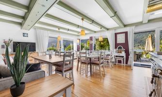 A bright and inviting living space with large windows and wooden beams. Stylish furniture and a beautiful view of nature make the room cozy and welcoming.