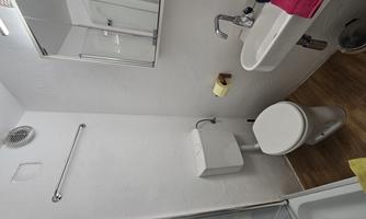 A modern bathroom with a toilet, a small sink, and a mirror. The walls are light, and there is a shower area.
