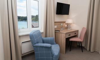 A cozy room with a blue armchair and a desk. The window offers a view of a beautiful lake with trees in the background.