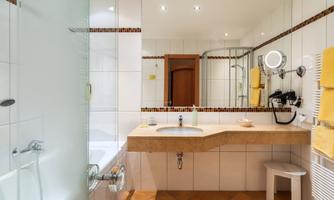 A modern bathroom with a glass shower room and a large mirror. Towels in yellow complement the friendly atmosphere.