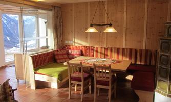 A cozy living space with wooden paneling and a dining table in the middle. Seating areas with striped cushions and plenty of daylight from the windows.