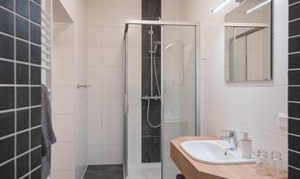 A modern bathroom with a glass shower and a wooden vanity. The walls are painted in neutral colors, with an elegant black accent.