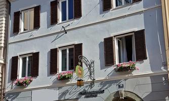 A pretty building with a blue facade and brown shutters. Blooming flower boxes adorn the windows.