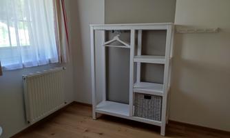 A bright room with a white wardrobe. The wardrobe has an open shelving unit and a laundry basket.