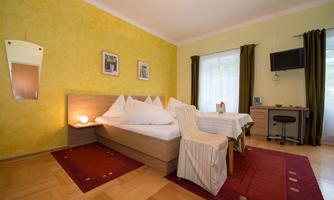 A cozy room with a double bed and yellow walls. A table with chairs is next to the window, and a small television is mounted.