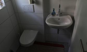 A small, modern bathroom with a sink and a toilet. Bright tiles and a window provide light.