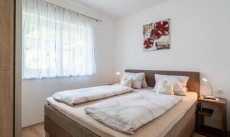 A cozy bedroom with a double bed and bright, natural light sources. On the wall hangs a picture of red flowers.