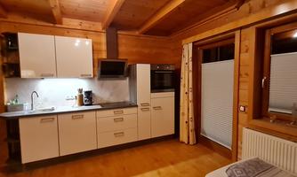 A modern kitchen with wood paneling and white furniture. It is well-equipped with appliances and has large windows for plenty of natural light.