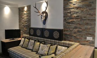 A modern living room with a cozy sofa and decorative pillows. A deer head hangs on the wall, and there is a television as well as natural stone elements.