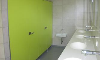 A modern bathroom with green partition walls and a white sink. There are several sinks with shiny faucets.