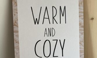 A sign with the inscription "WARM AND COZY". It has a nice, simple frame and conveys a cozy feeling.
