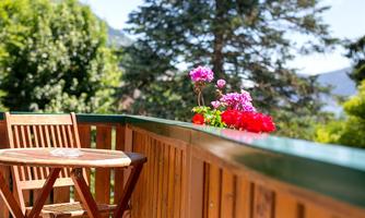 A beautiful balcony with a wooden table and chairs. Colorful flowers bloom in pots and in the background, green trees can be seen.