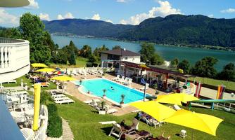 A beautiful pool area with loungers and sun umbrellas. In the background, you can see a picturesque lake and mountains.