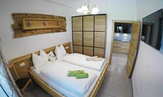 A modern bedroom with a double bed and two light pillows. The walls are in neutral tones, and there is a large wooden wardrobe.